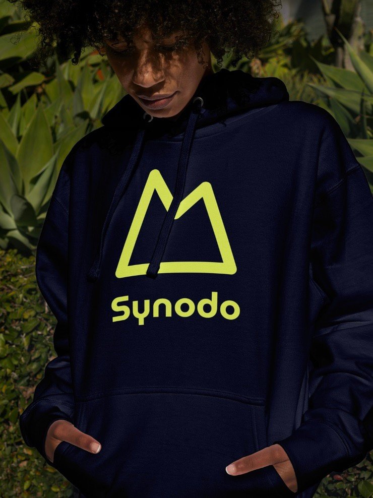 Fotografía de una persona vistiendo un buzo con capucha color azul oscuro que lleva estampado el logotipo de Synodo en amarillo neón.