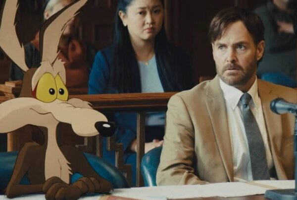 Escena de tribunal híbrida de acción real y animación de la película Coyote vs. Acme, mostrando al personaje animado Wile E. Coyote sentado en la mesa de la defensa junto al actor Will Forte, quien interpreta a su abogado, con el jurado al fondo