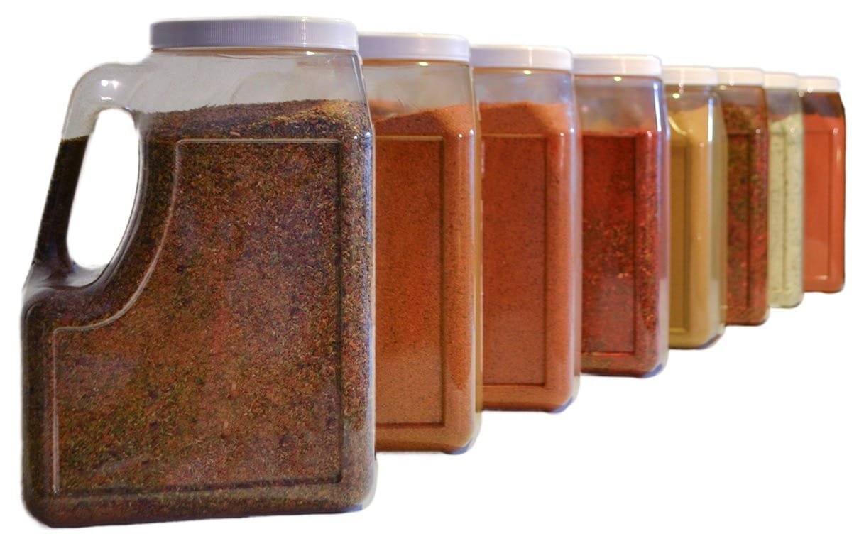 Fila diagonal de grandes jarras de plástico de estilo comercial o de servicio de alimentos llenas de diversas especias molidas, incluidas hierbas verdes, pimentón naranja y curry marrón para uso al por mayor