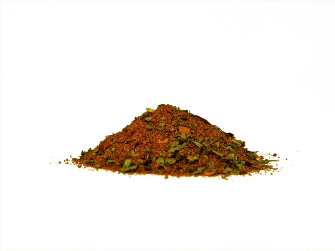 Vista frontal a nivel de superficie de un montón de condimento con textura gruesa, compuesto por especias naranjas y trozos de hojas verdes