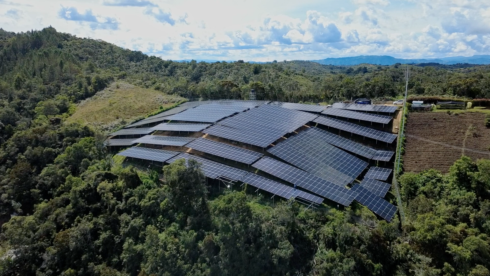 Largas filas de paneles solares reflejando el cielo azul y las nubes en un entorno montañoso rural, captura de producción para video corporativo de Solenica.