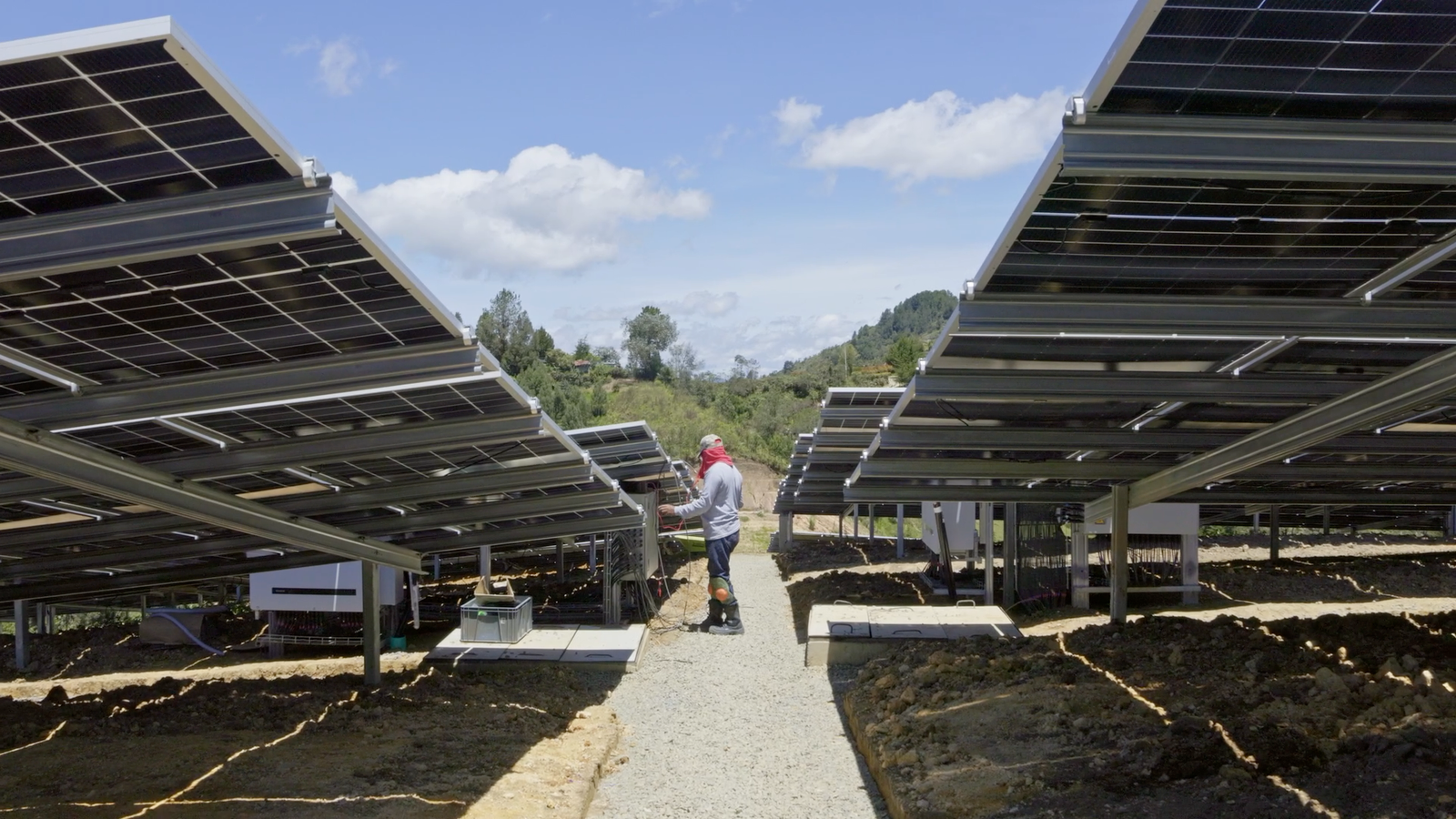Trabajador con equipo de protección realizando labores de cableado y mantenimiento bajo las estructuras de los paneles solares.